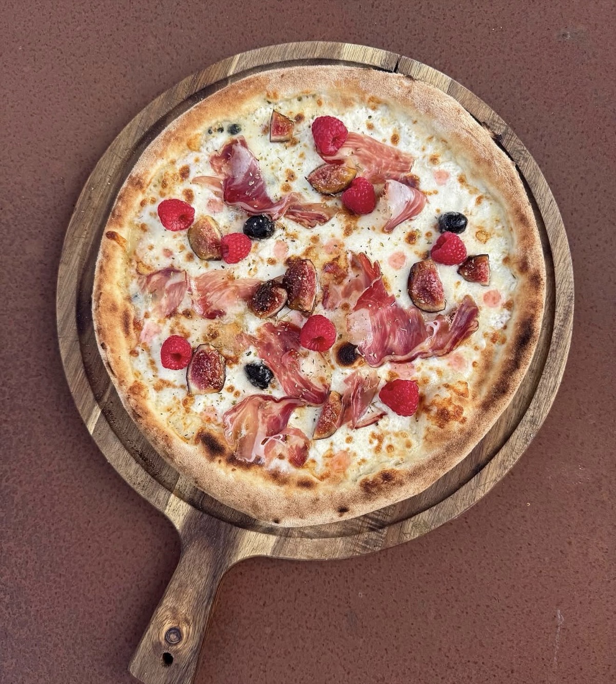 Pizza figues, framboises et prosciutto sur planche en bois